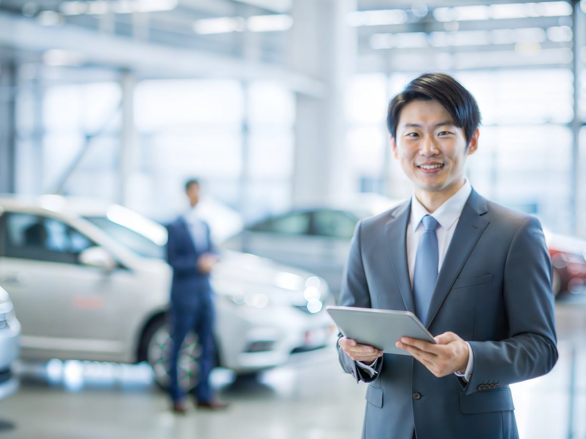 自動車ディーラーのショールームでタブレットを持つ営業担当者